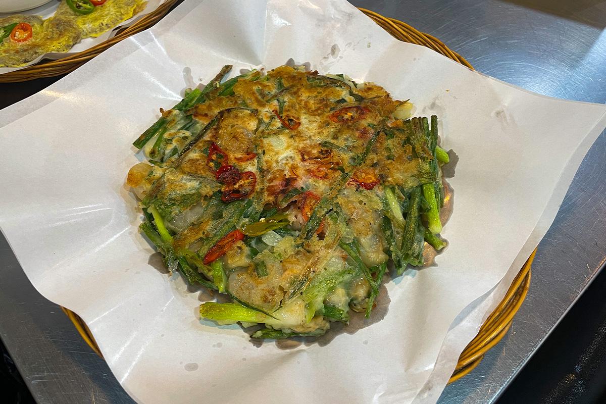 Ein Meeresfrüchte-Lauch-Pfannkuchen, zubereitet im Gwangjang-Markt in Seoul, garniert mit roten Chilischoten.