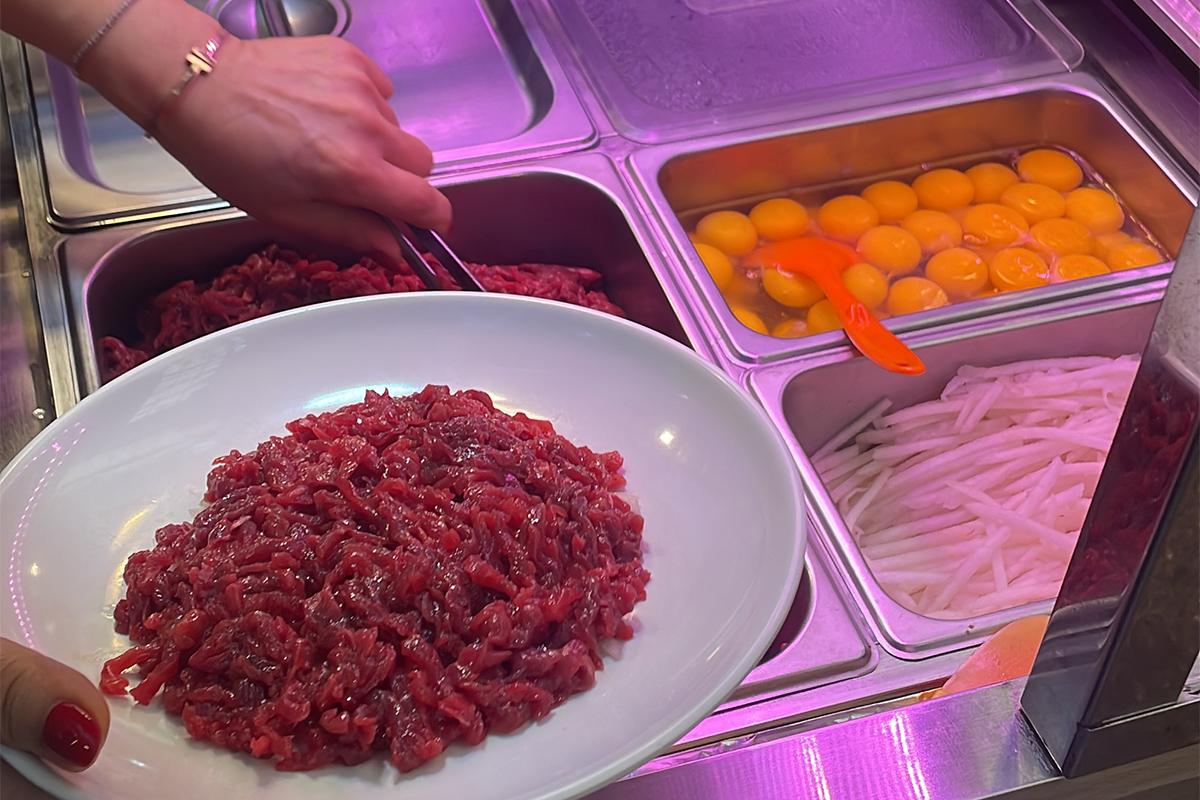 El proceso de preparación de Yukhoe en Bakgane Yukhoe en el Mercado Gwangjang, mostrando el cuidado en el emplatado.