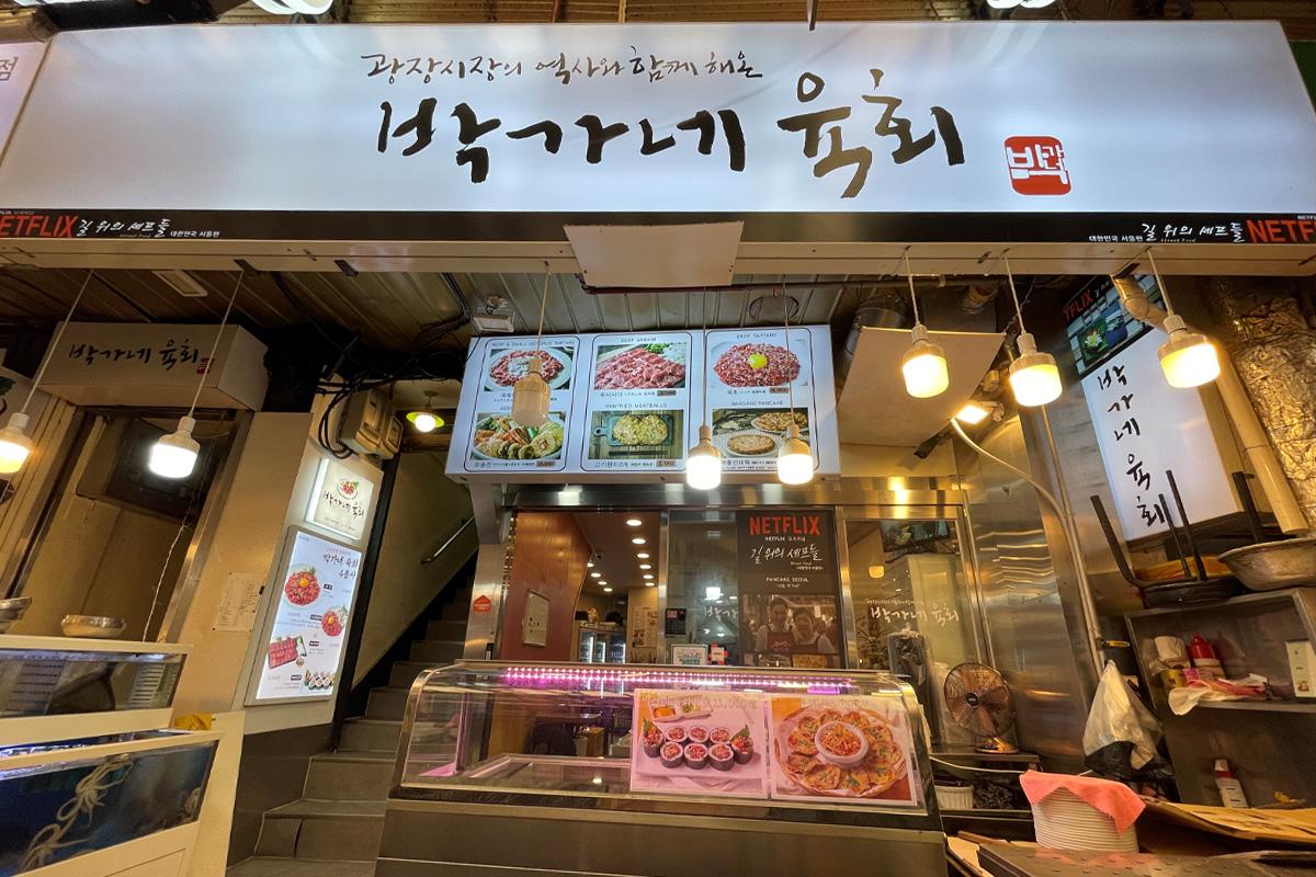 Fachada del restaurante Bakgane Yukhoe en el Mercado Gwangjang, famoso por su Yukhoe, con imágenes de su aparición en NETFLIX.