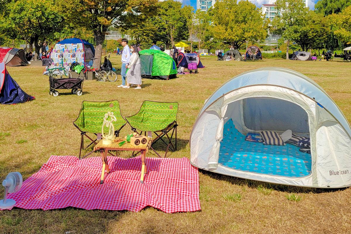 Cozy camping-style picnic setup with a tent, table, and colorful chairs set up under bright skies.