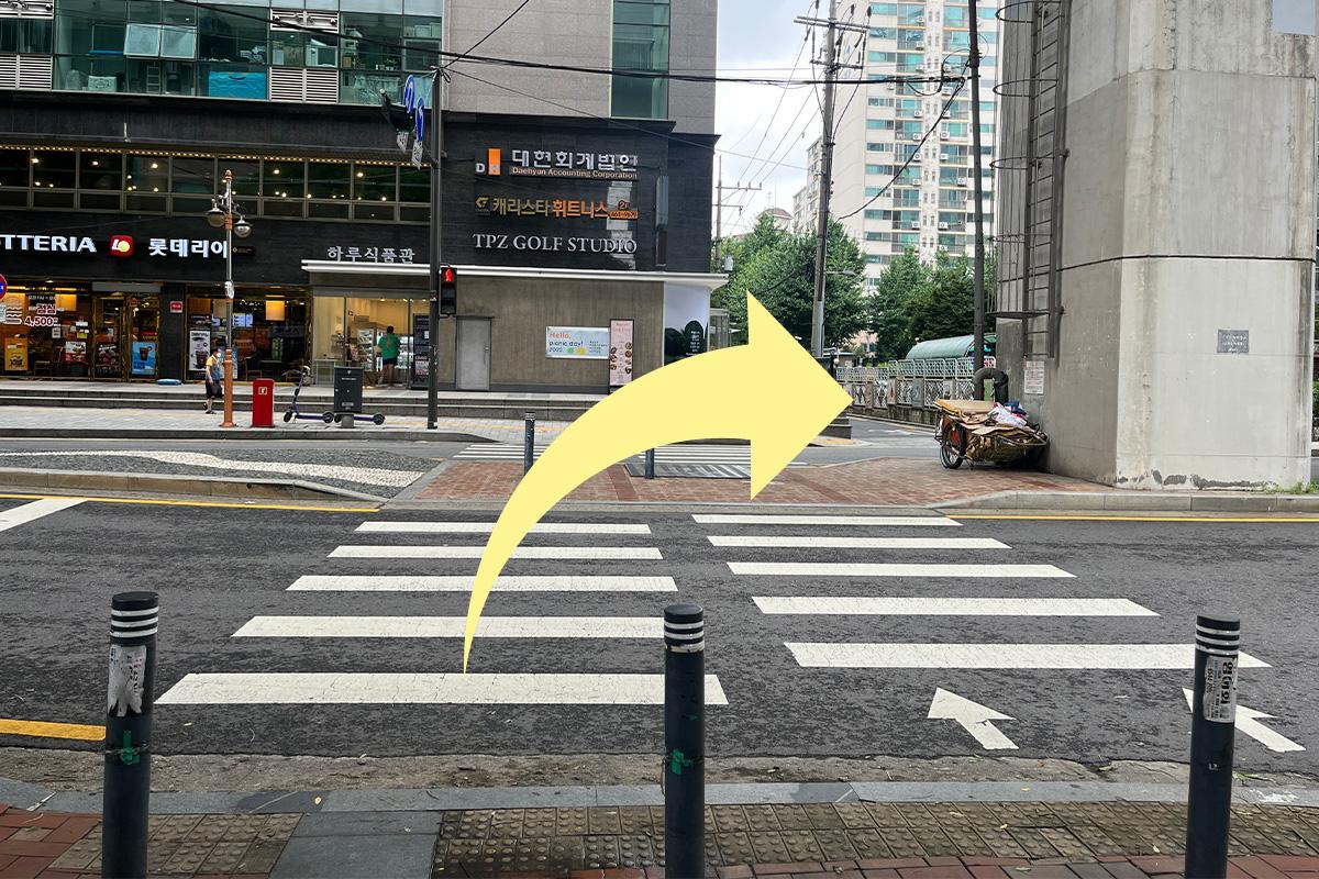 Crosswalk near a commercial area with a directional arrow, leading towards the Han River in Seoul.