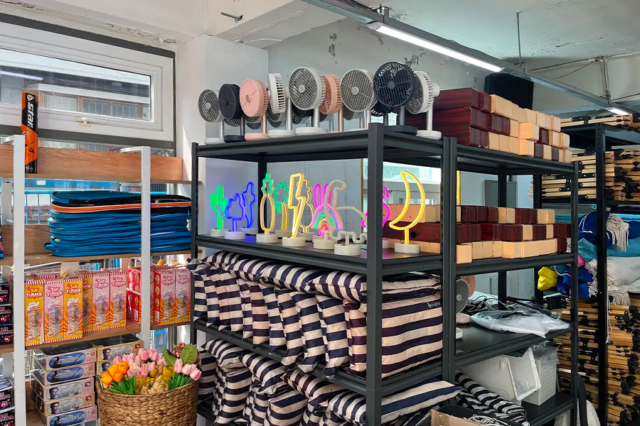 有色彩斑斕裝飾燈具的架子，展示了多樣化的露營和野餐用品，包括風扇和條紋墊子。