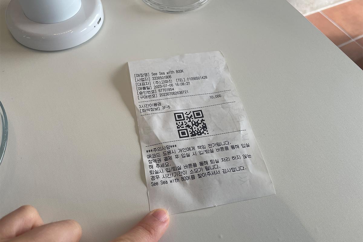 Квитанция с QR-кодом для входа в Sea Sea with Book, лежащая на столе в кафетерии.
