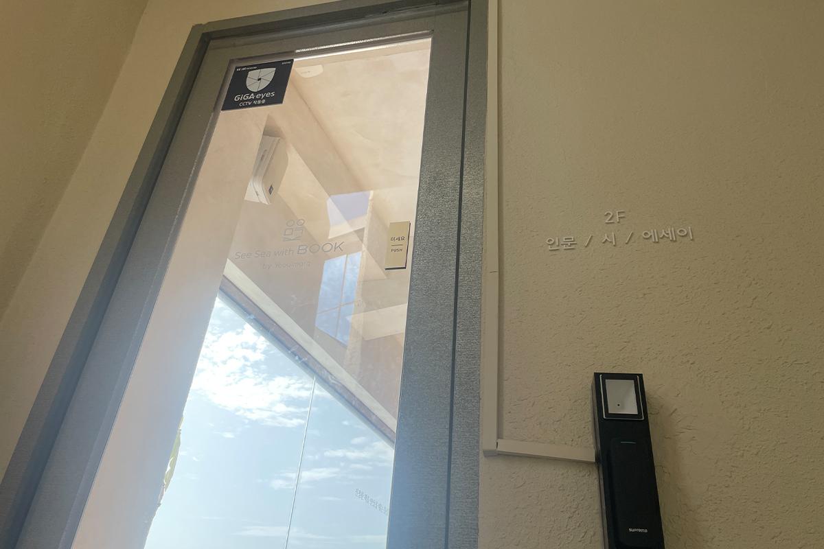 Вход на второй этаж кафе Sea Sea with Book с стеклянной дверью и видом на небо.