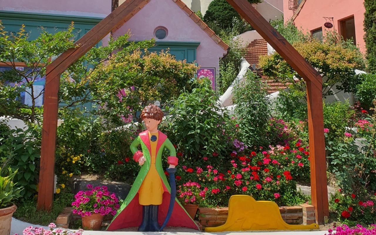 Charming Little Prince statue amidst vibrant flowering plants in Petite France, perfect for a picturesque memory.