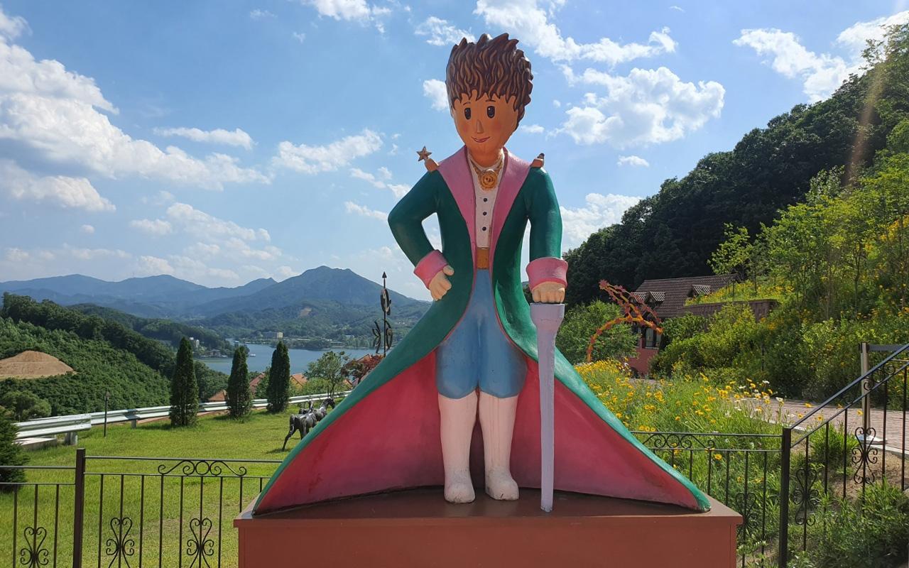 Colorful statue of The Little Prince at Petite France, surrounded by floral landscapes and mountainous views.