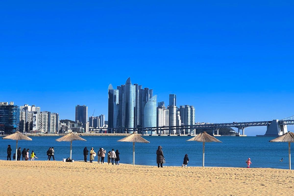 韓国の人気旅行地、釜山の広安裏海水浴場の美しい風景。ビーチには訪問者が訪れ、背景には高層ビルと広安大橋が見える。