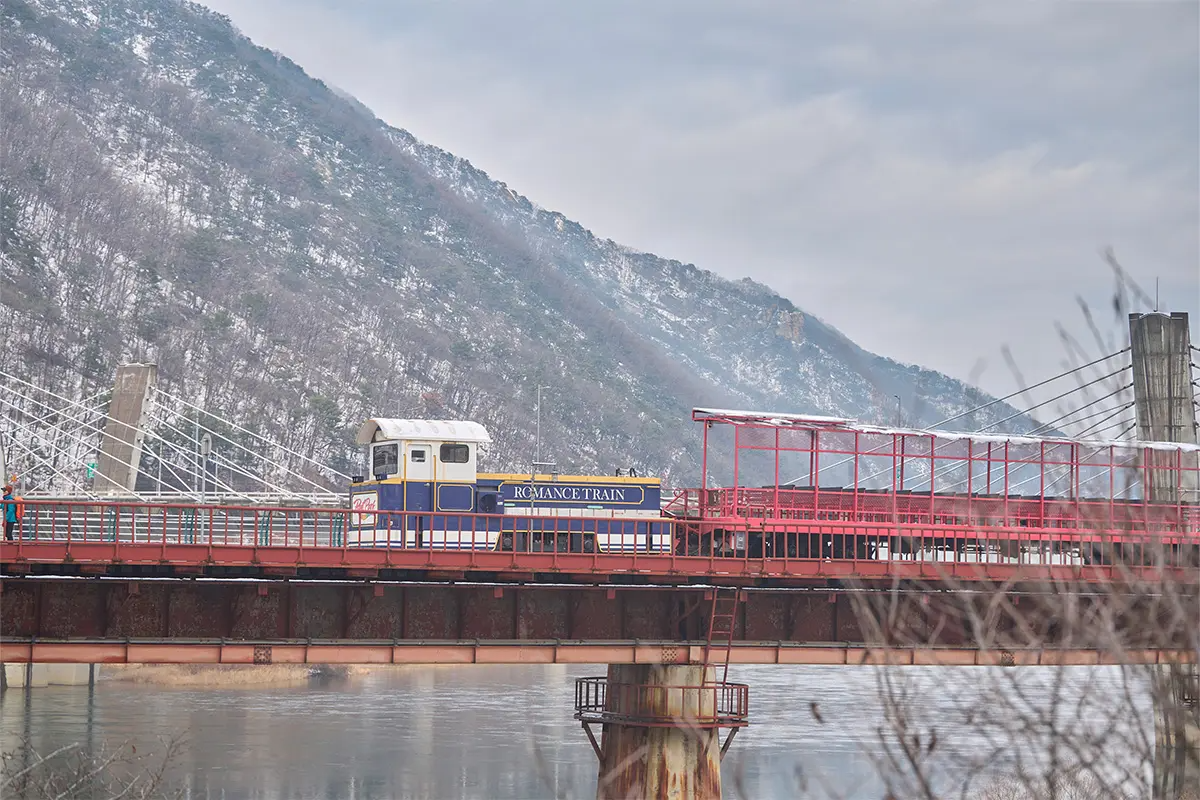 Tren romántico del tour en bicicleta de riel en Corea, cruzando un puente en invierno bajo montañas nevadas.