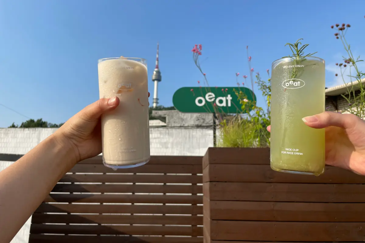 Zwei erfrischende Getränke werden auf der Terrasse des Oeat Cafés angehoben, mit Namsan Tower im Hintergrund.