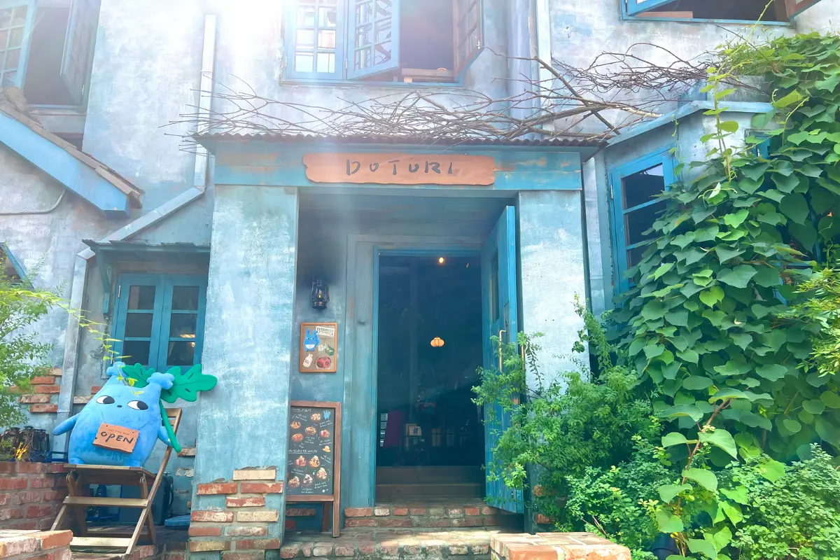 Äußeres des Dotori Cafés mit blauen Wänden und einem malerischen Eingang, umgeben von viel Grün.