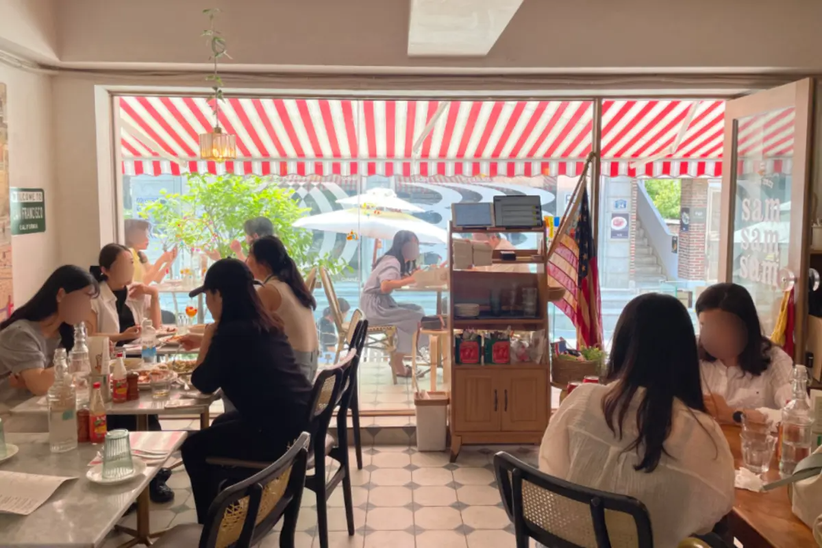 Innenansicht des Sam Sam Sam Restaurants mit Gästen, die an Tischen unter einem gestreiften Pavillon sitzen.