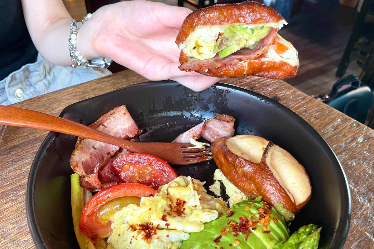 Brunchplatte im Dotori Café mit gestapeltem Laugenbrot, Gemüse, Speck und Eiern.