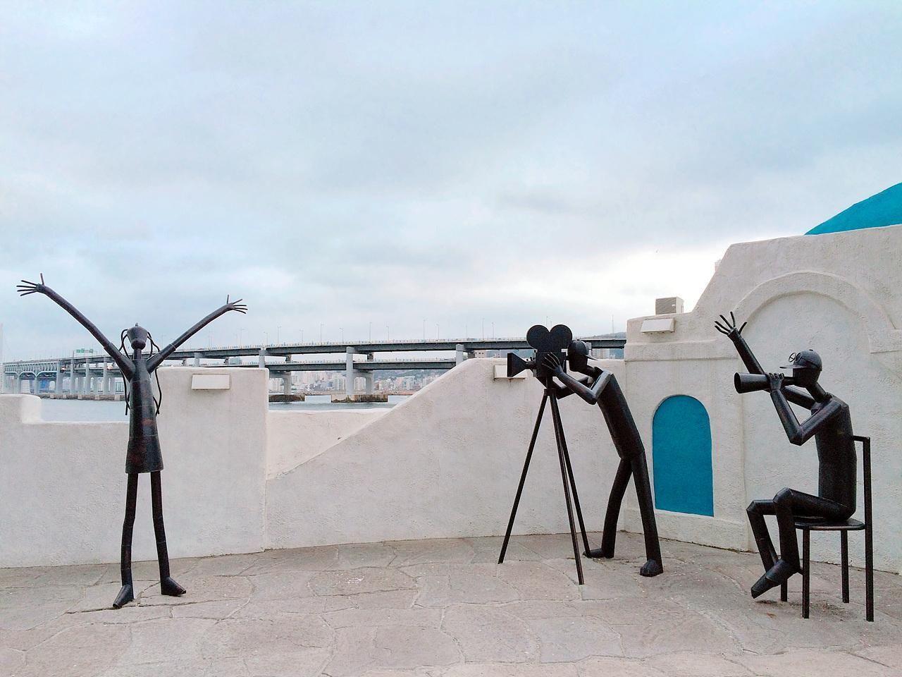 Interactive film-related sculptures on Movie Street in Busan's Haeundae, against a backdrop of Gwangan Bridge.