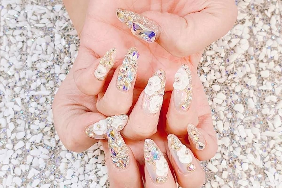 Beautifully ornate nail art featuring white and crystal embellishments on a customer's hands.