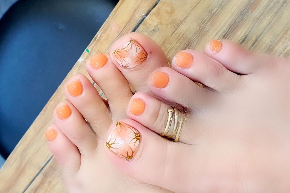 Elegant pedicure with orange nail polish and floral nail art design on the toes.