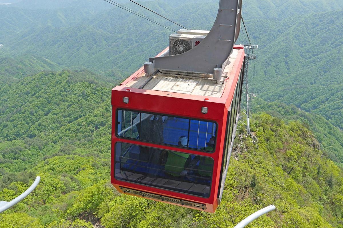 Baekamsan-ийн кабель машин. Кабельт машин нь улаан өнгөтэй бөгөөд ой модтой уулын дээд хэсгээс явж байна.