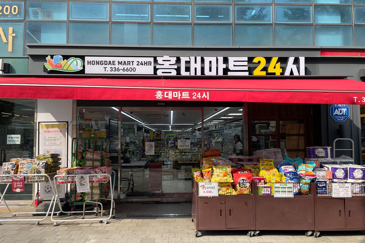 Front view of Hongdae Mart 24 Hours with various snacks and goods displayed outside the store.