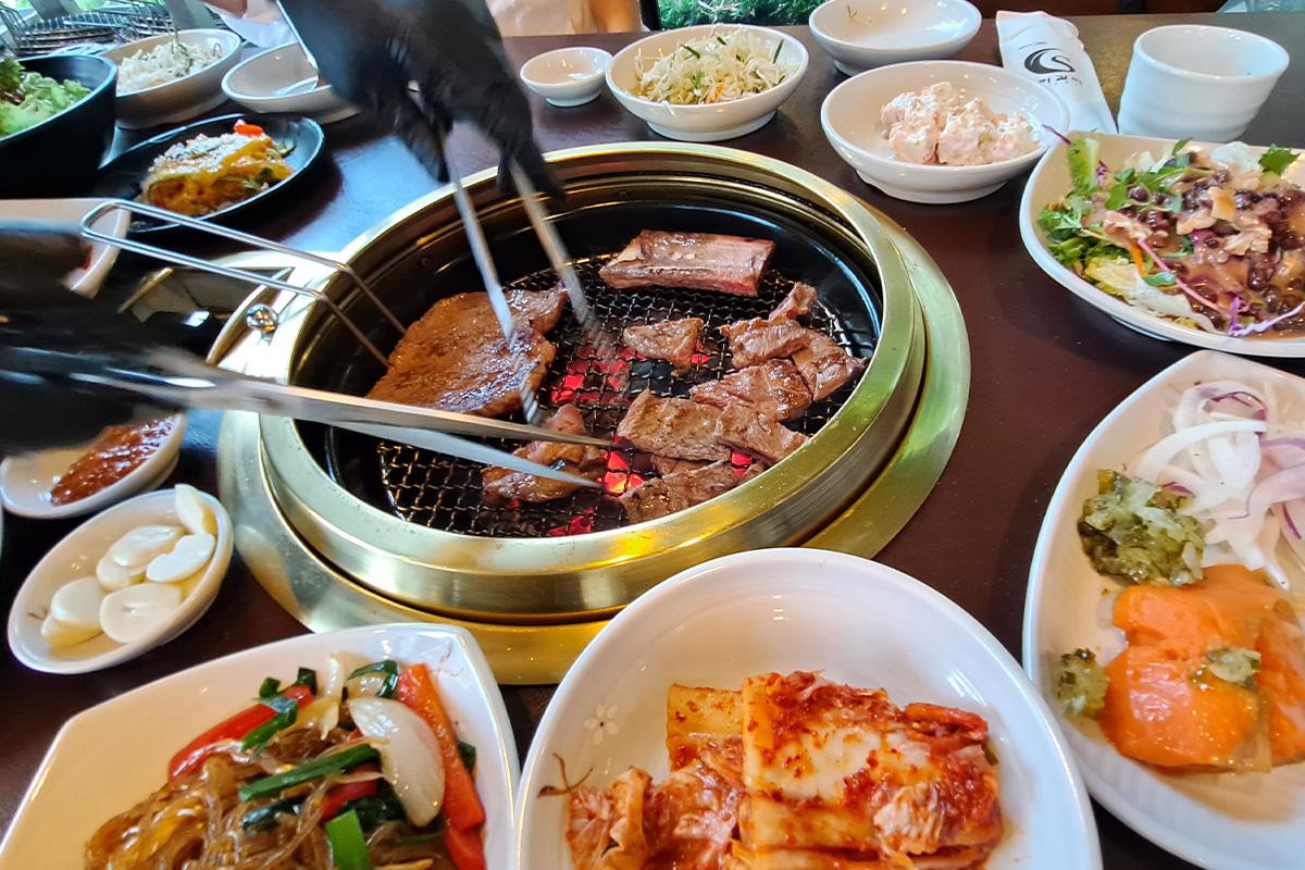 Suwon Galbi zubereitet über Holzkohlegrill mit Beilagen.
