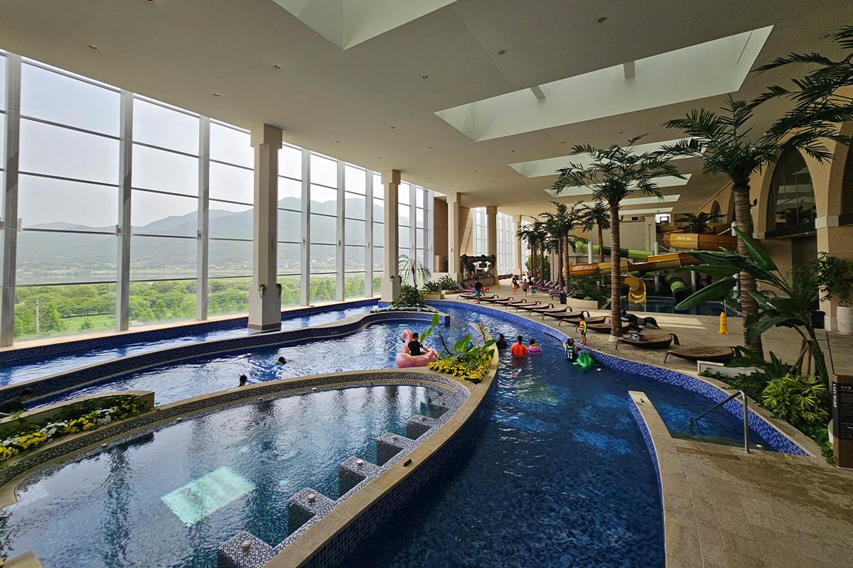 Panoramic view of Aqua Field indoor water park with large windows and palm tree decor