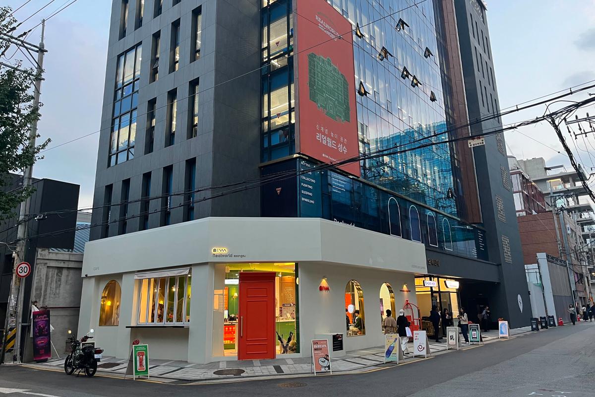 韓国旅行 ソウル 聖水 駅からのアクセスルートの様子。建物を背景にしたRealworldの鮮やかなオレンジの入り口、ソウルの街の一角に位置していることを示す.