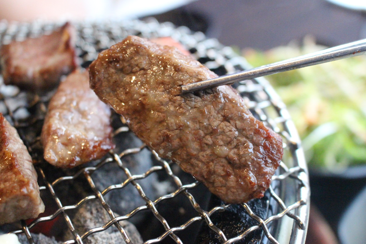 用夹子夹起的火气爱爱建大本店的烧烤牛肉片，展示出肉质多汁。