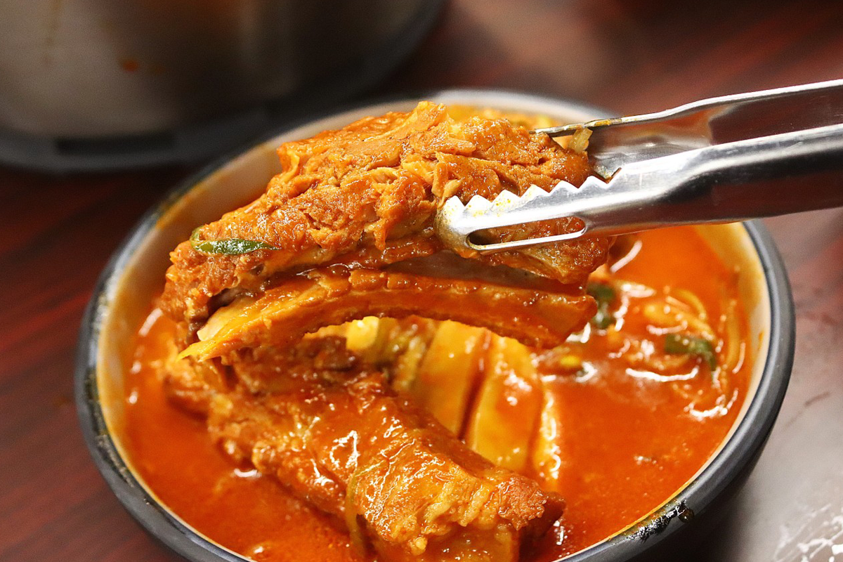 使用夹子夹起청춘등판店中的炖排骨，展示其软嫩的肉质。