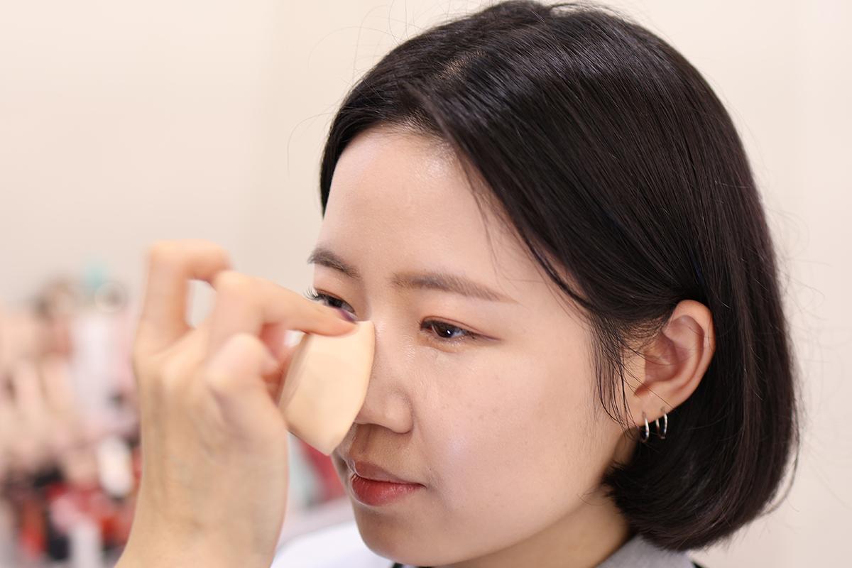 化妝師正在進行眼影塗抹,演示眼部化妝技術,顯示其專業性。