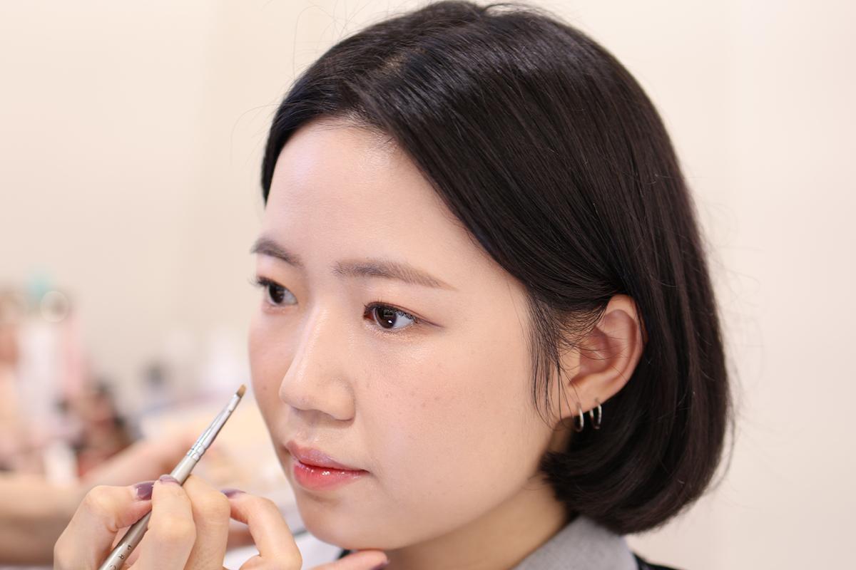 化妝師正在進行腮紅和唇妝修飾,展示了腮紅的敷上及均勻刷過技術。