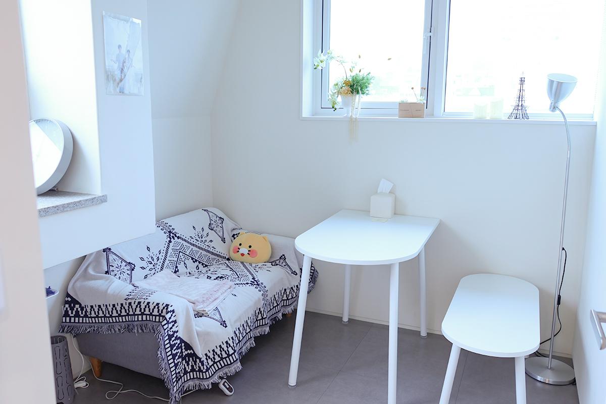 等候區,一張放有可愛玩偶的沙發和白色桌椅,舒適的空間設計,窗外有自然光照射。