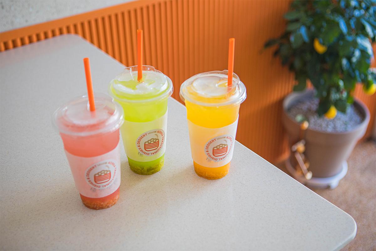 Three refreshing fruit-flavored beverages at BIBIBIM cafe in Busan, displayed on a table with vibrant colors including pink, green, and orange.