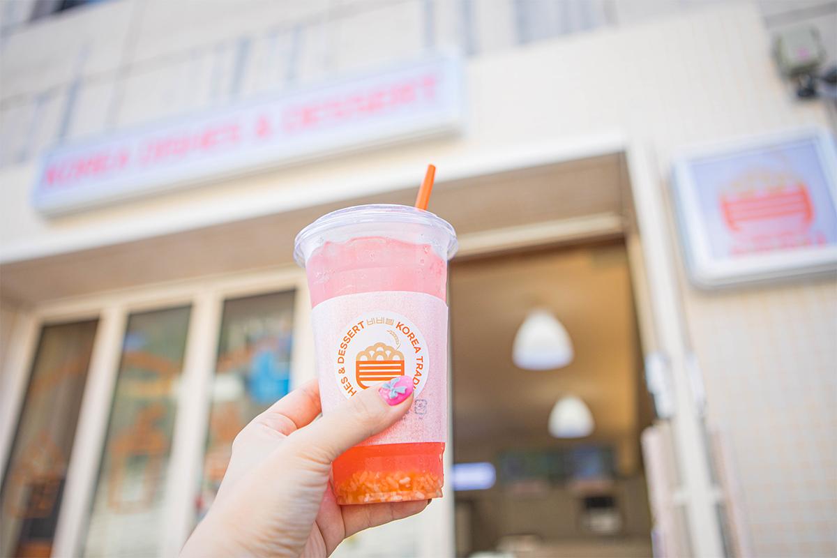 A tempting fruit beverage held up against the backdrop of BIBIBIM cafe's entrance sign, perfectly illustrating the vibrant drink choices available here.