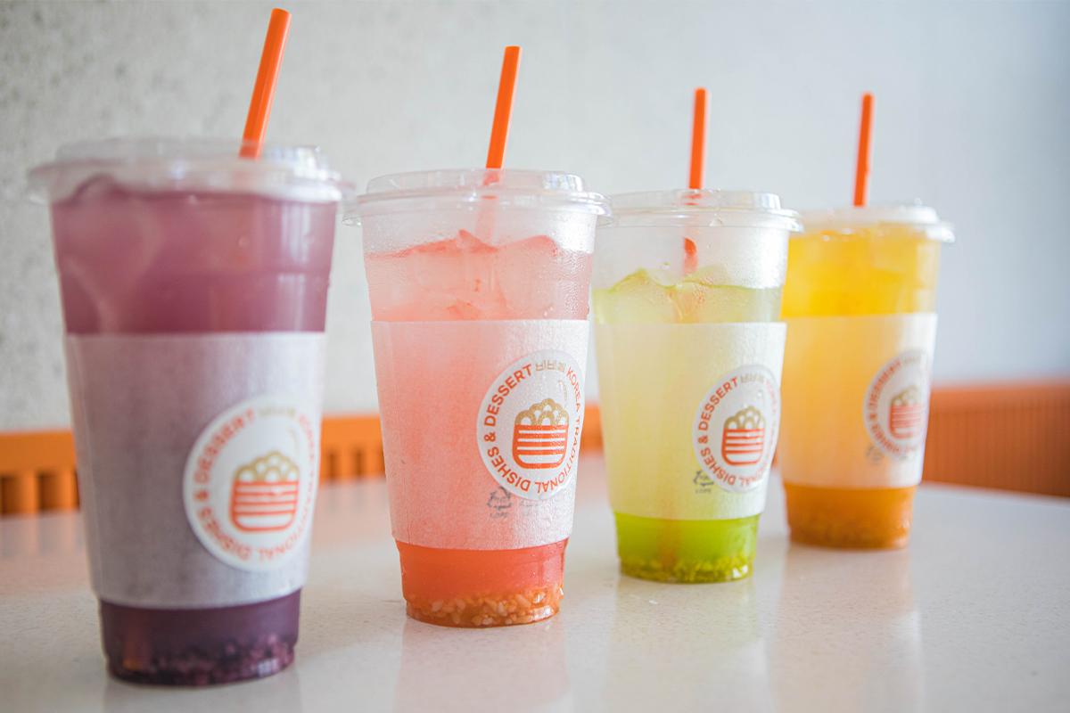 Four colorful, fruit-flavored drinks lined up on a table at BIBIBIM cafe near Gamcheon Culture Village, in hues of purple, pink, green, and yellow.