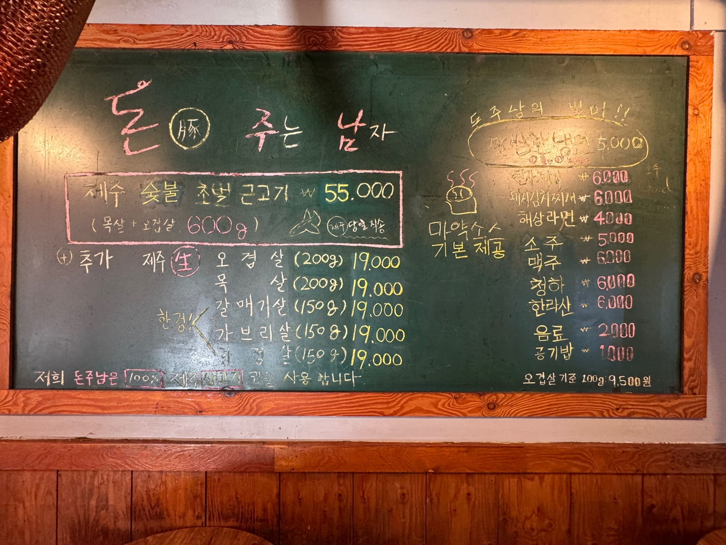 弘大濟州燒肉店、給豚的男人，菜單展示牆面上的選項包括直送濟州炭燒豬肉、豚泡菜湯及冷麪等菜品，店內環境温馨，充滿懷舊風格。適合品味韓國特色燒肉料理的理想去處。