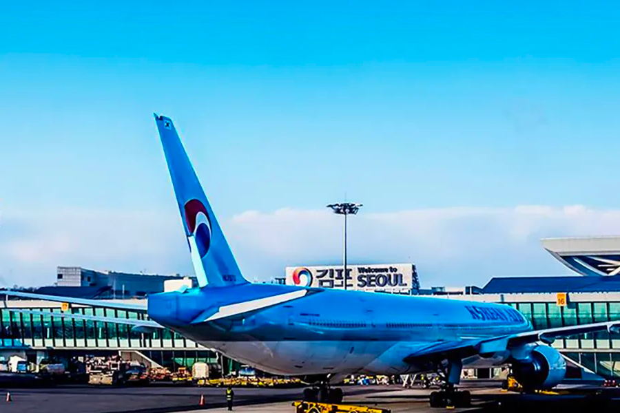 大帽子的一家人在機場，背景顯示航線及航班信息，包含釜山航線，等待登機人群。