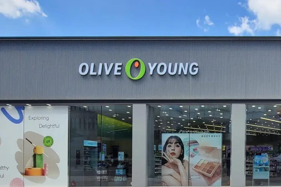 首爾街景中的 Olive Young 美妝藥妝店外觀，晴天藍天下的店招與落地玻璃櫥窗，適合介紹6月購物折扣與旅遊行程建議。