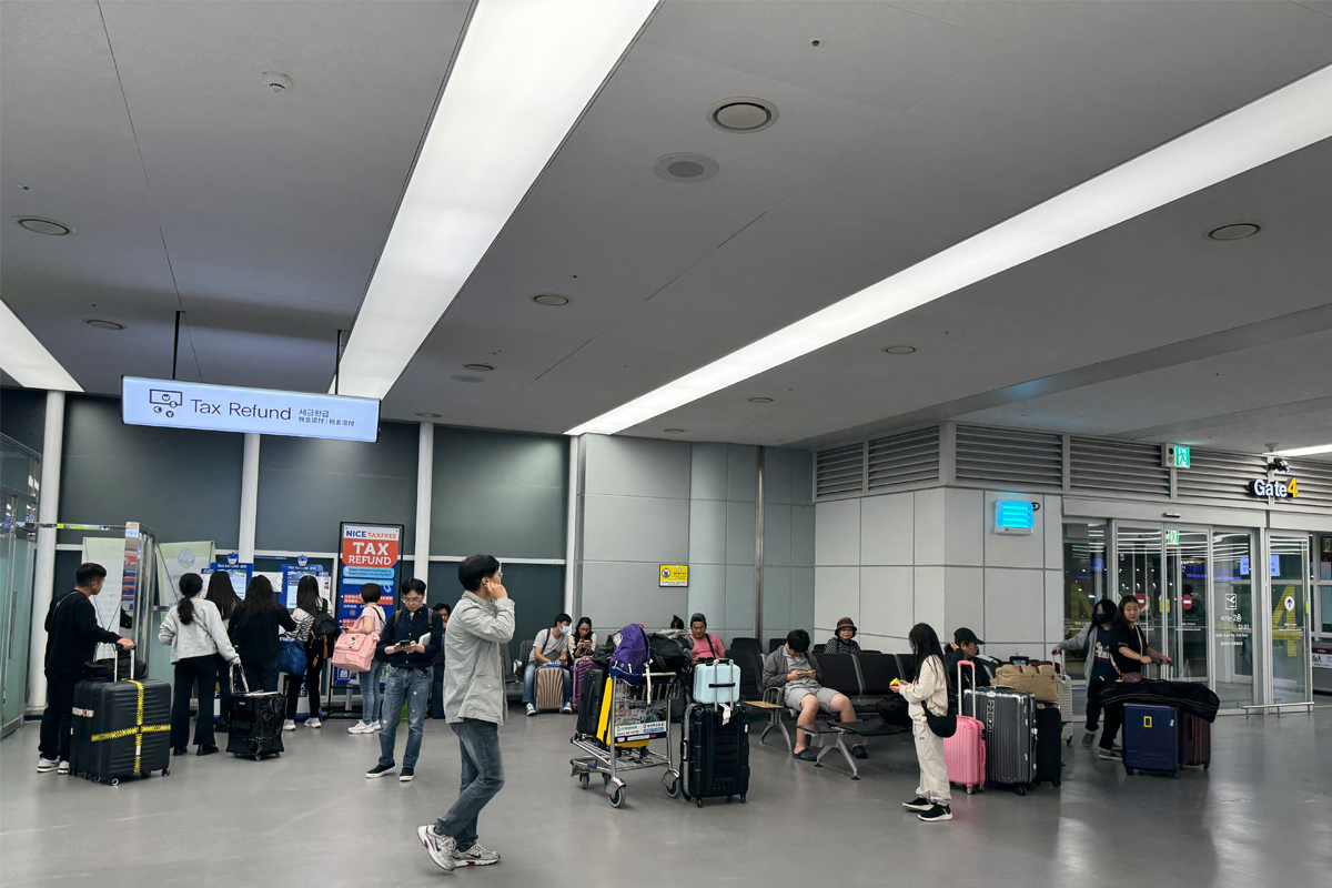 釜山金海機場退稅區域，旅客聚集在退稅機旁，處理退稅手續