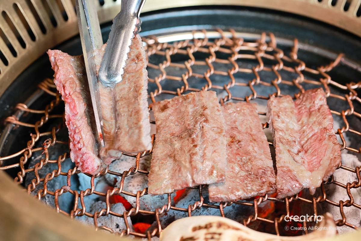 正在烤的牛排片，被烤夾夾住，呈現完美的脆皮