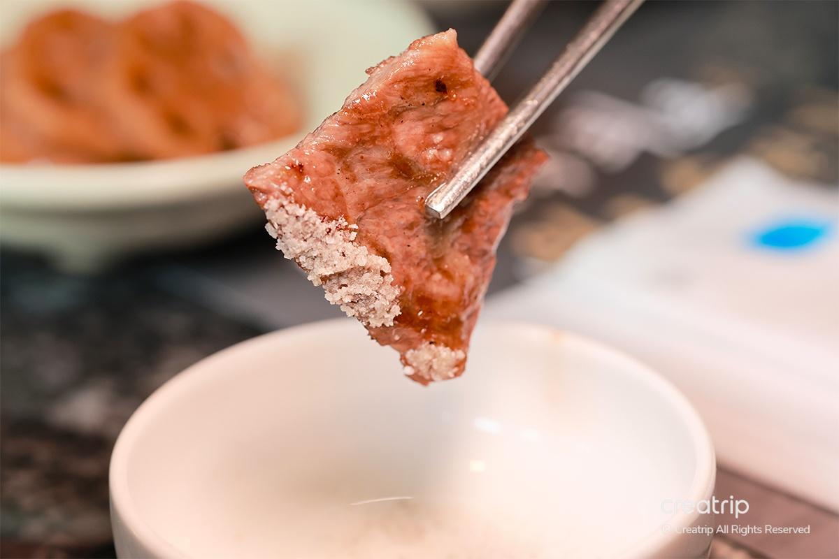 沾有鹽的牛肉片被筷子夾住，準備入口