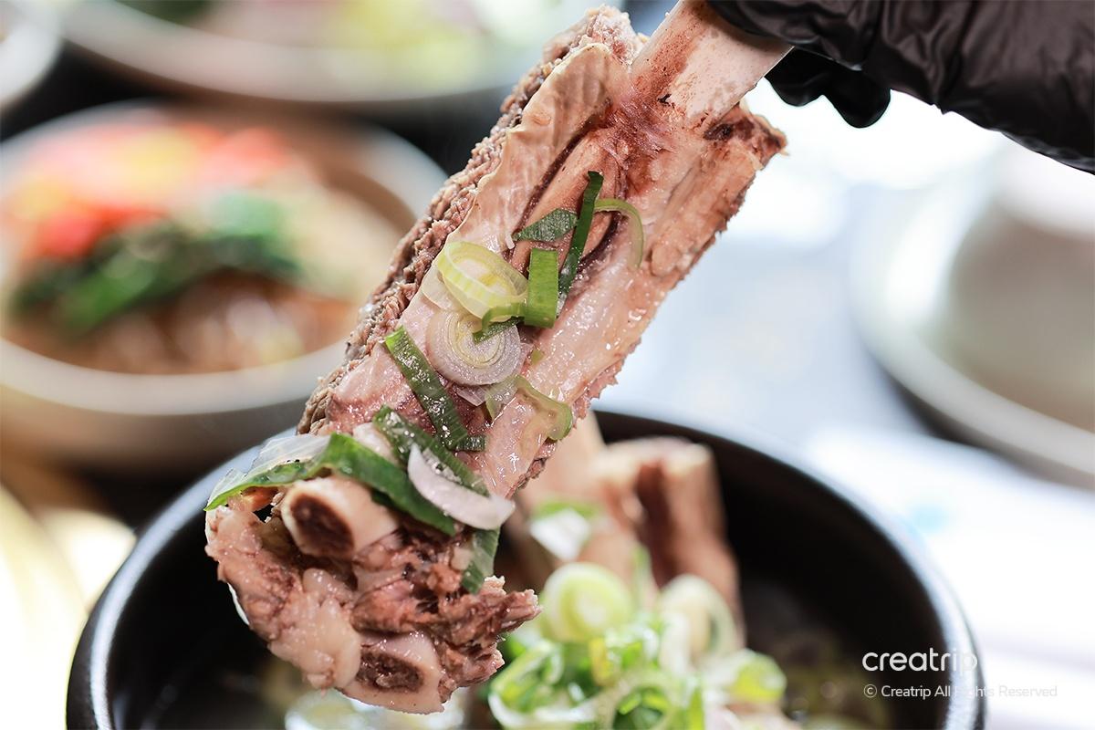 從牛排骨湯中舉起一塊牛肉，展示其嫩肉和上面的蔥花