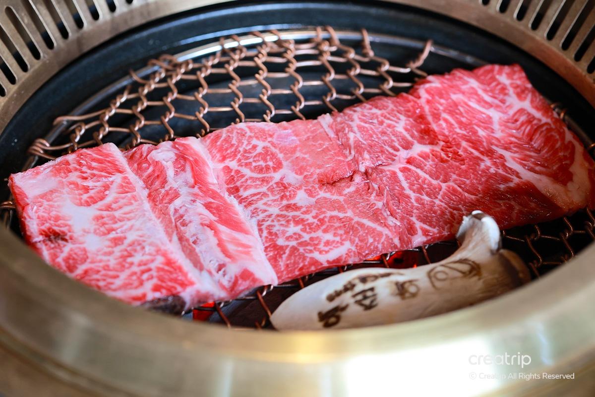 華春屋的牛排肉放在烤架上，烤架上還有香菇