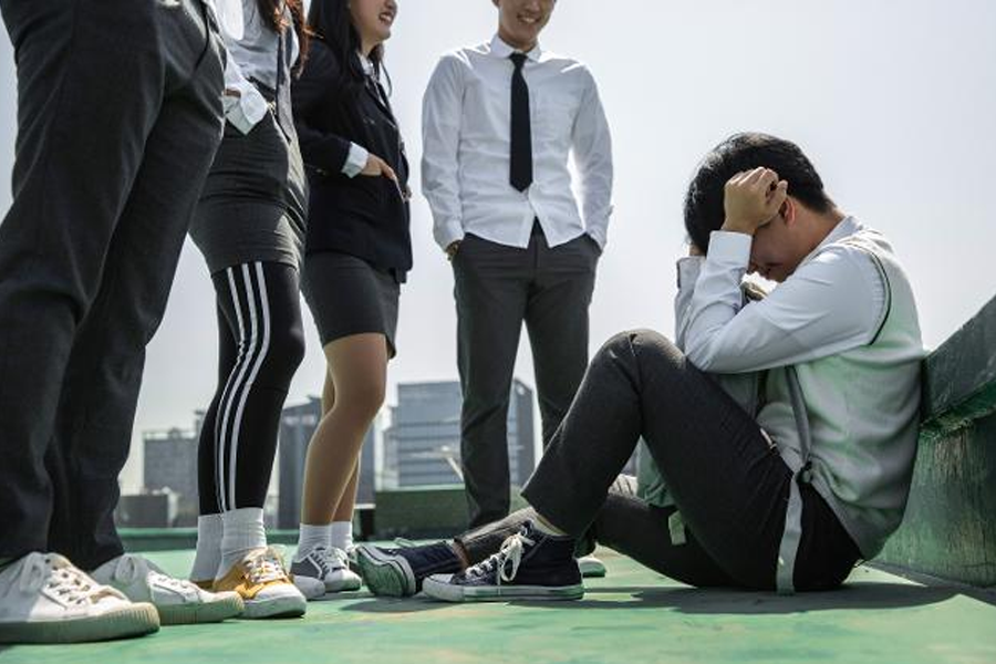 韓國校園屋頂場景：數名學生聚集在一起，一名孤獨的學生抱著頭蹲坐在地上，顯示出被欺壓的情況。