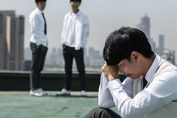 韓國校園屋頂場景：一名孤獨的學生蹲在前景，兩名男學生站在遠處，隔著距離佔有優勢。