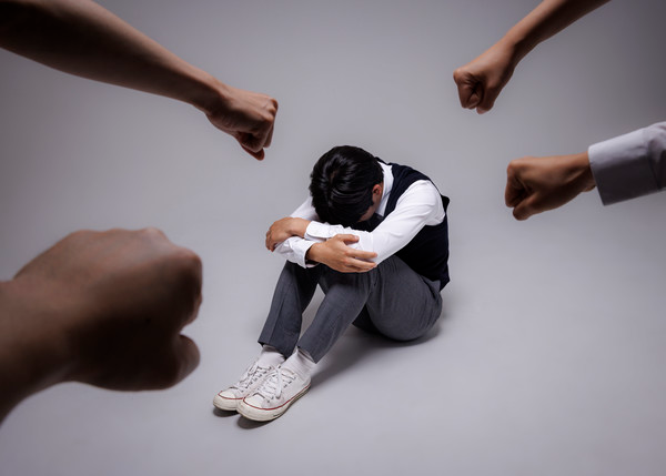 韓國校園霸凌場景：一名學生低著頭蹲坐在地上，周圍環繞著數名學生的拳頭，表現出霸凌行為的壓力。