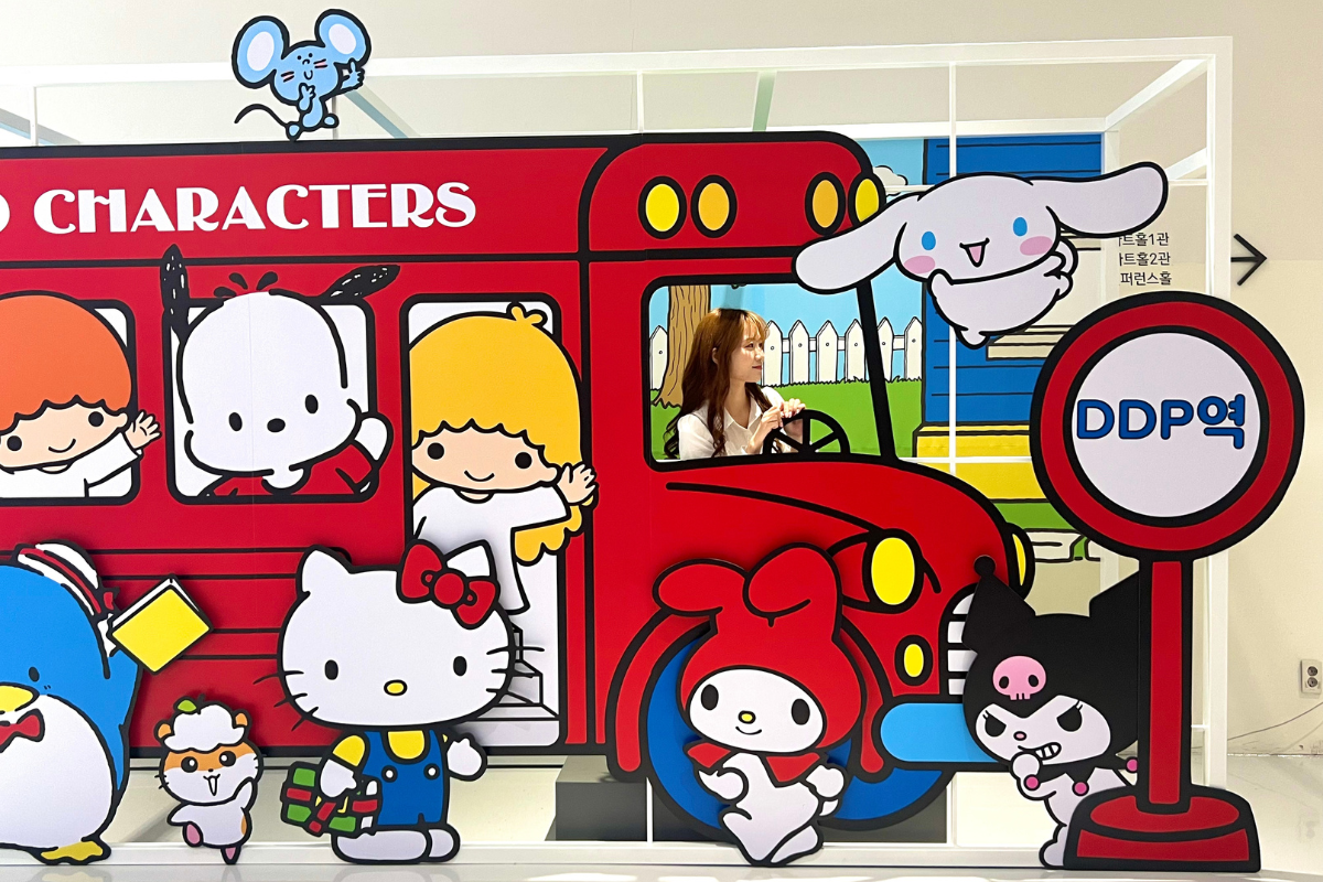 ハローキティ50週年特別展のフォトスポット、バスやサンリオキャラクターが描かれた背景が特徴です。