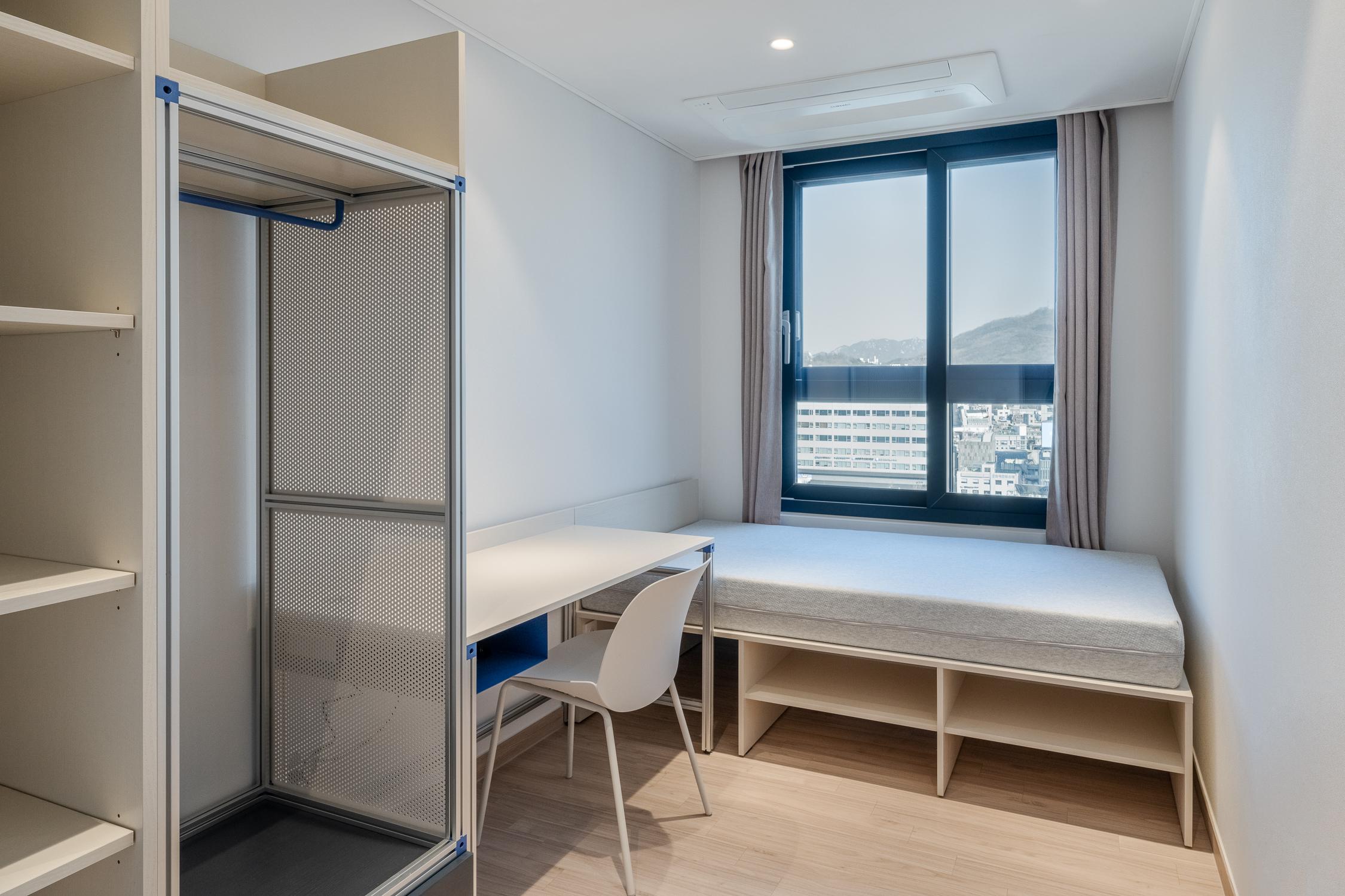 ภาพห้องพักประเภทหนึ่งใน Co-living House Mangrove Sinchon ซึ่งเป็นห้องเดี่ยวที่มีหน้าต่างขนาดใหญ่ เตียงเดี่ยวและพื้นที่ทำงานพร้อมเก้าอี้