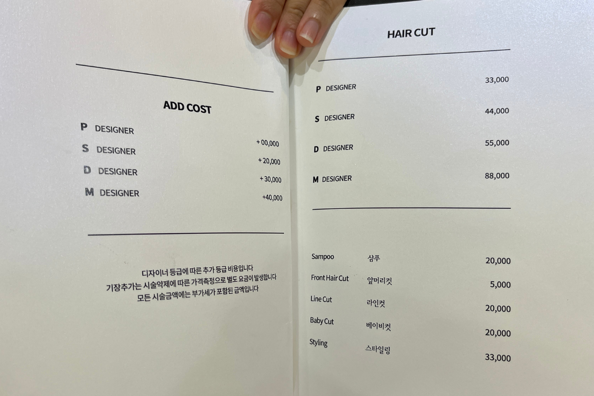 Menu dei prezzi in un salone di parrucchieri coreano che mostra costi aggiuntivi in base all'esperienza del designer.