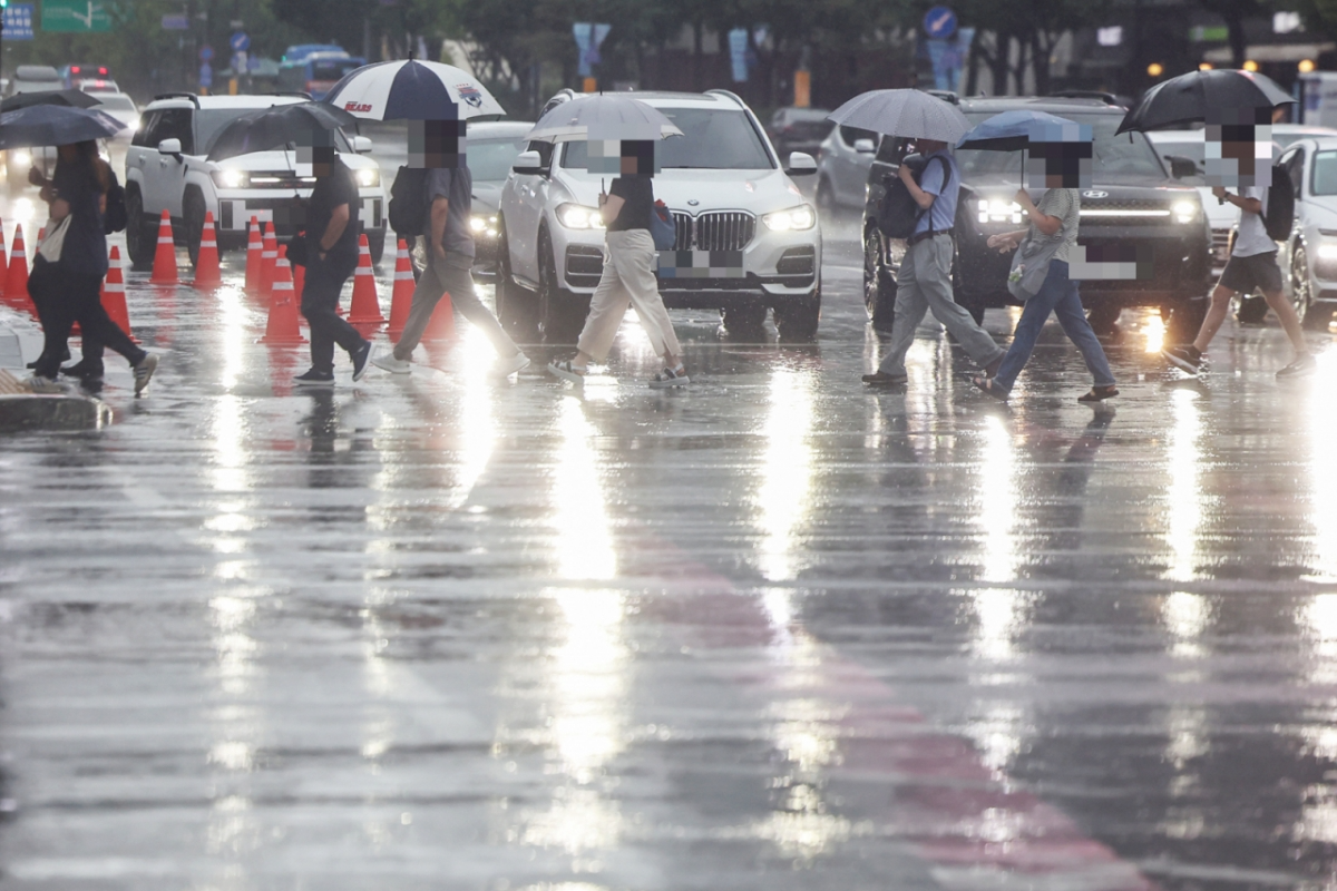 首爾街頭梅雨季行人撐傘過馬路，濕滑路面映出車燈與人影，提醒旅客雨季出行需備傘、注意積水與交通延誤。