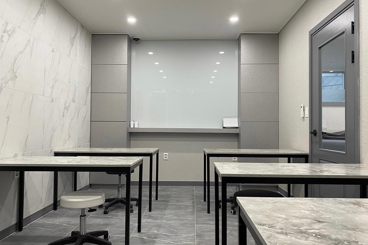 A classroom set up at KoResQ beauty academy, featuring tables, chairs, and a whiteboard.