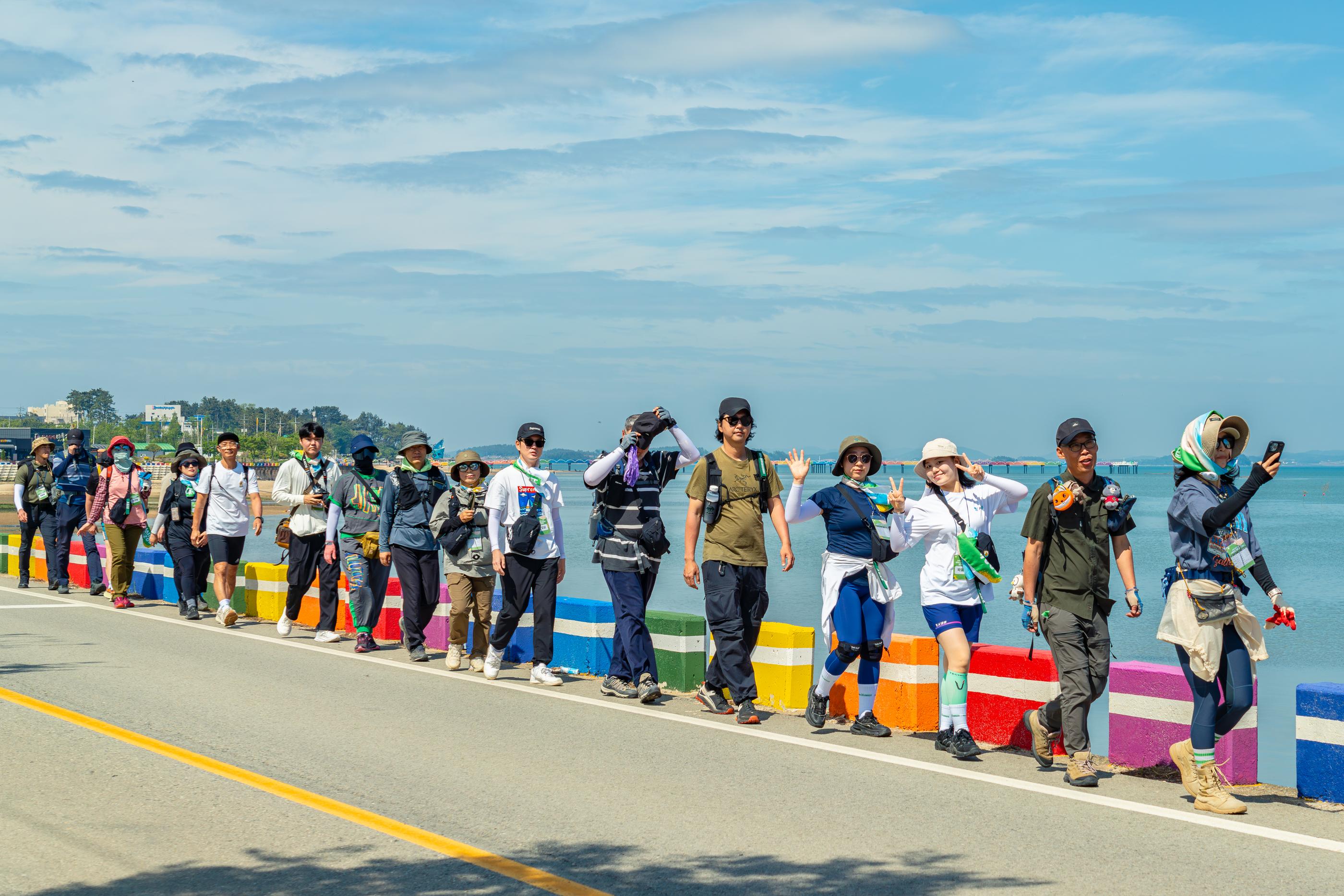 Colorful group of hikers walking along a sunny coastline on the Korea Dulle Trail.