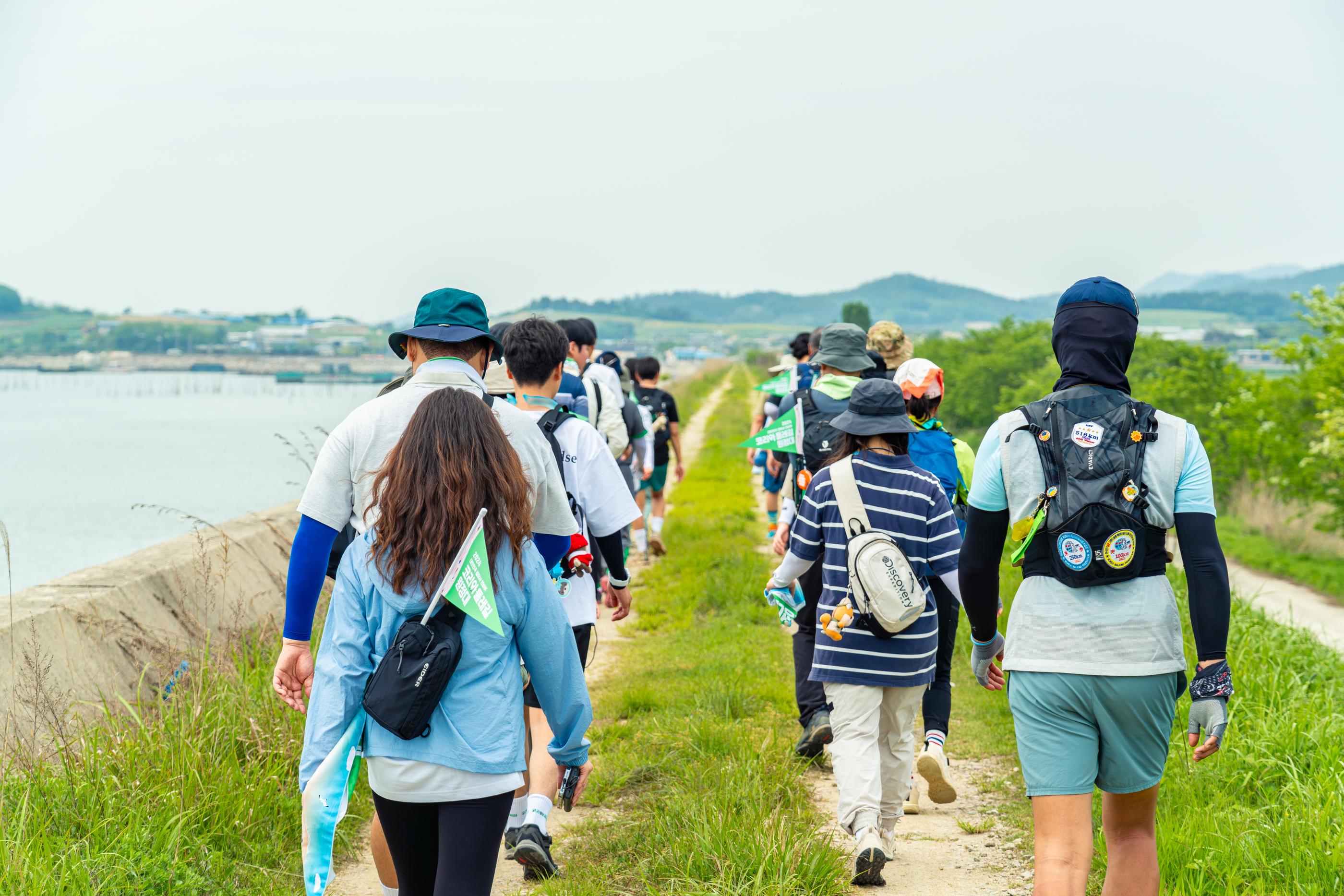 Group of hikers walking on a path along a lush coastline on the Korea Dulle Trail.